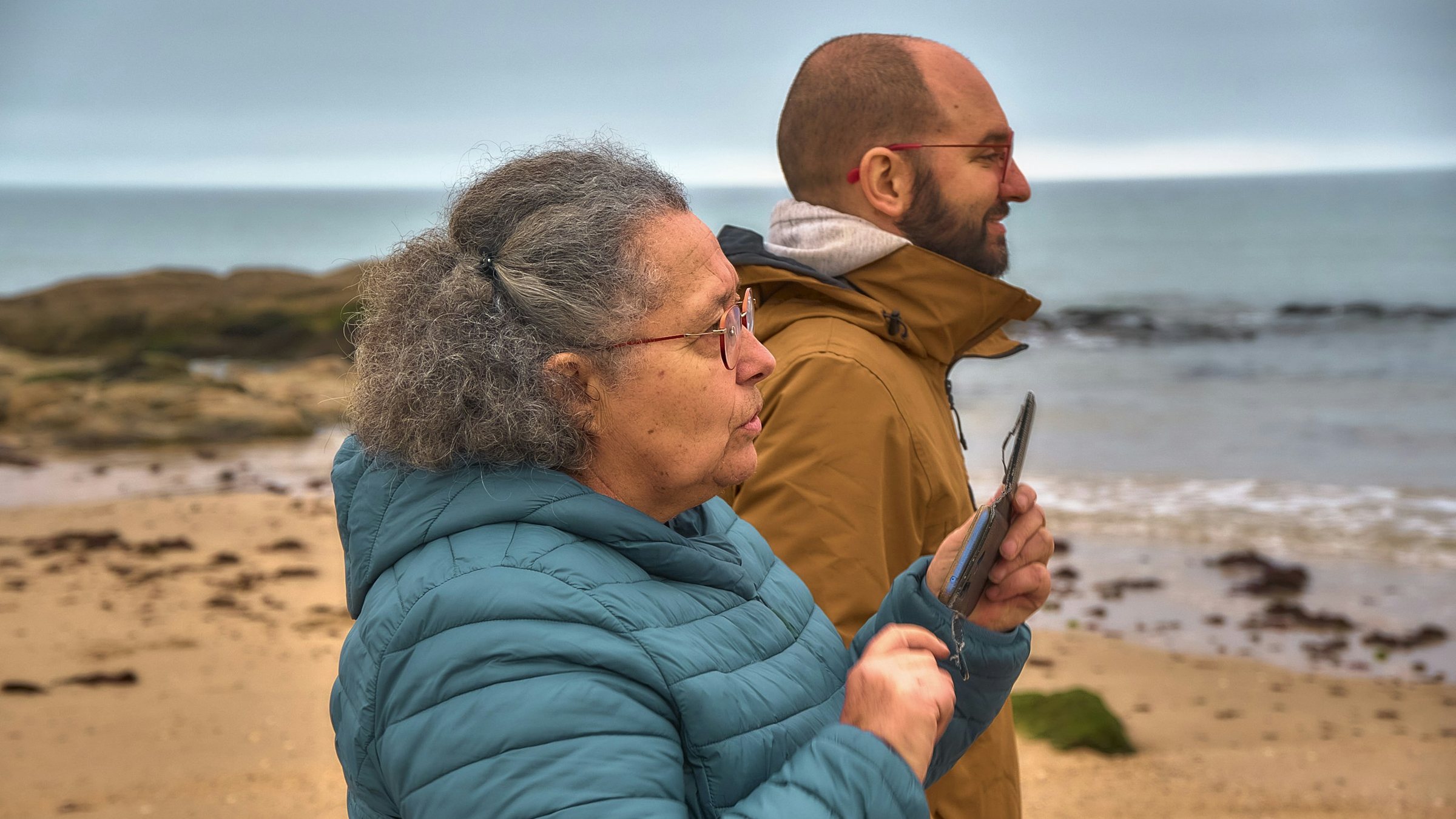 Una mujer camina junto al mar con el teléfono en la mano.