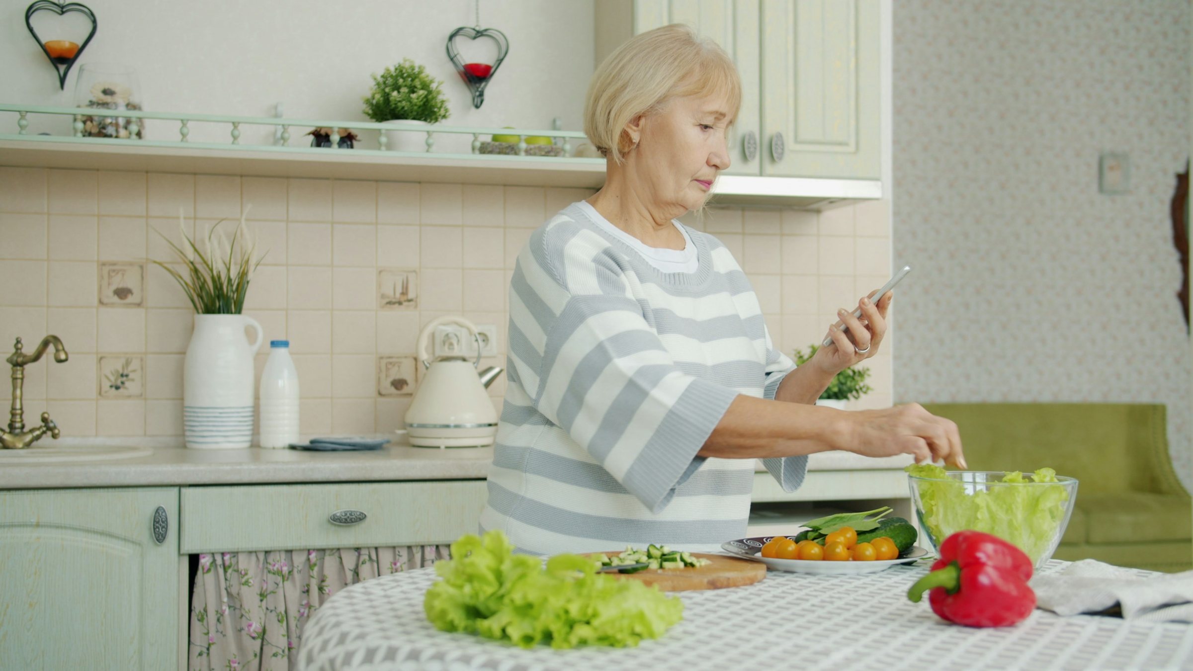Una mujer prepara una ensalada en casa y mira su teléfono.
